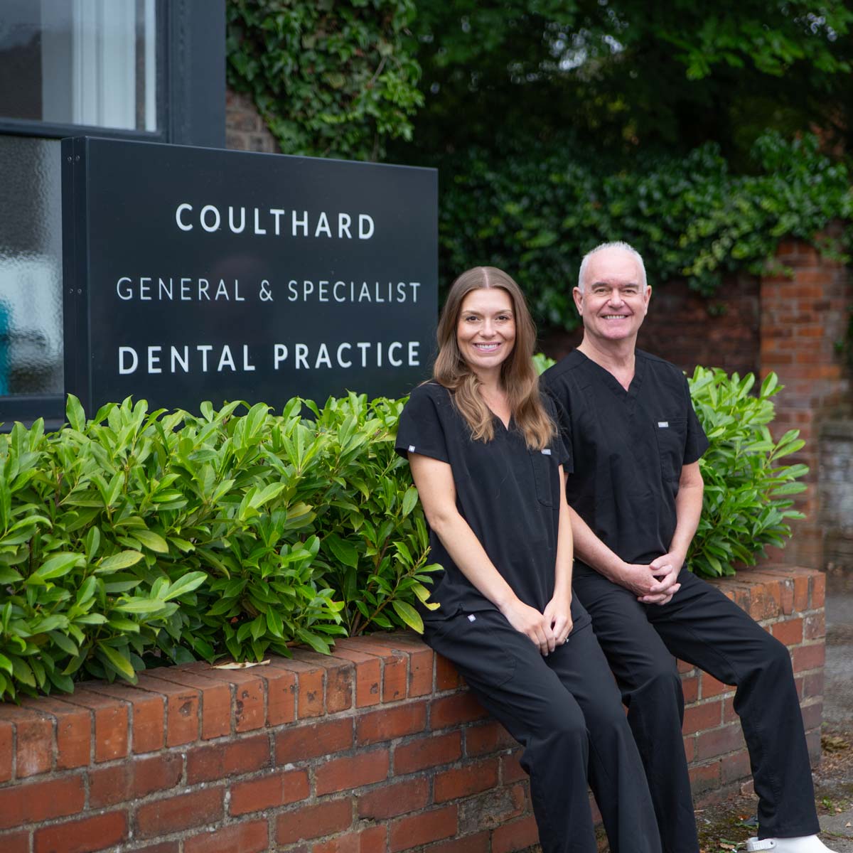 Dr Francesca Coulthard and Professor Paul Coulthard sit on a wall outside their family run dentist in Wilmslow